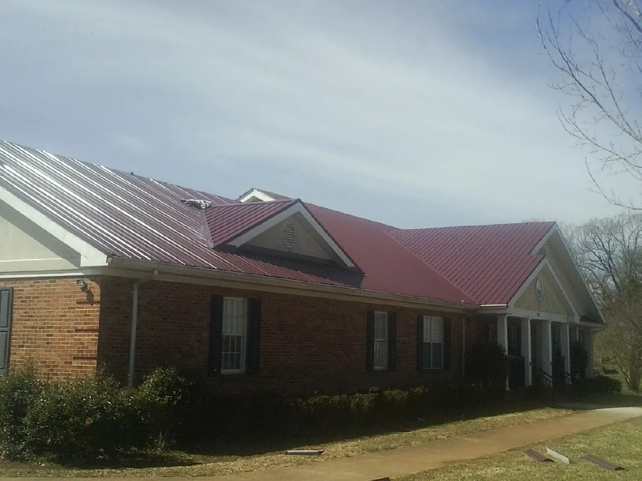 Red metal roof with gabled entries on a long brick building, from a Hail Damage Roof Repair job in Mannsville