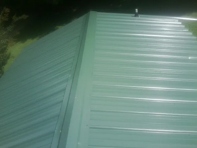 New green metal panels meeting at the ridge of a roof — Flat Roof Repair work by our crew in Mannsville