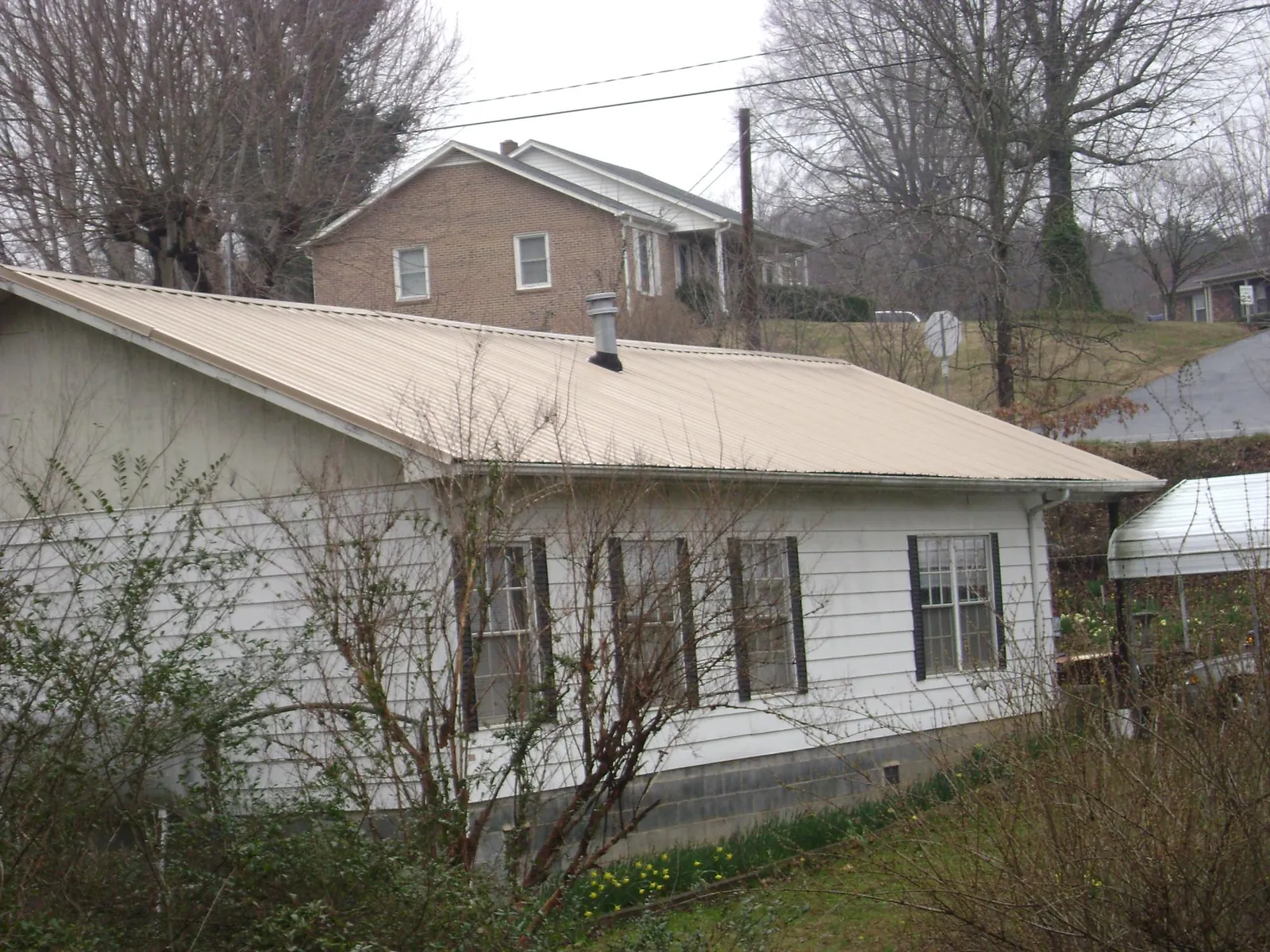 Tan metal roof on a white sided house set into a hillside — Commercial Roofing by Roofing Brothers in Mannsville