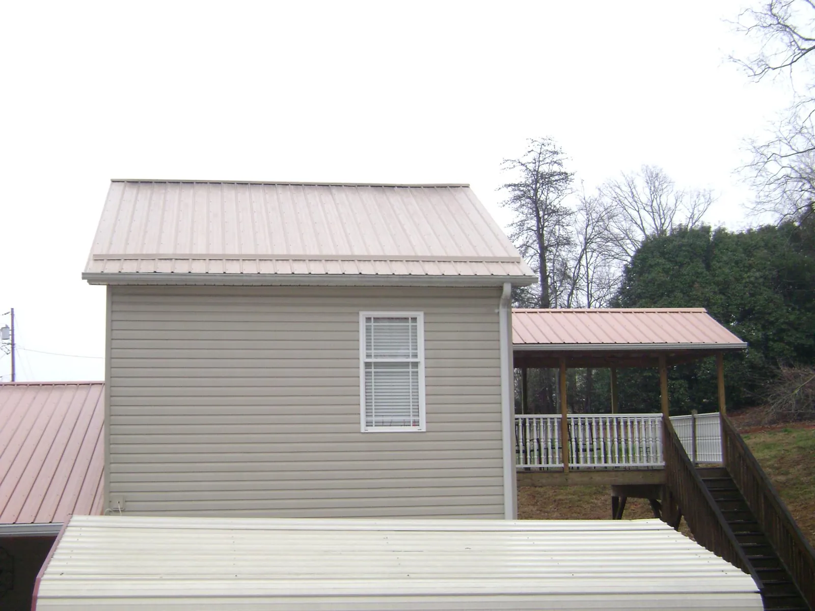Tan metal roofs on a two story addition and attached porch, from a Roof Replacement job in Mannsville